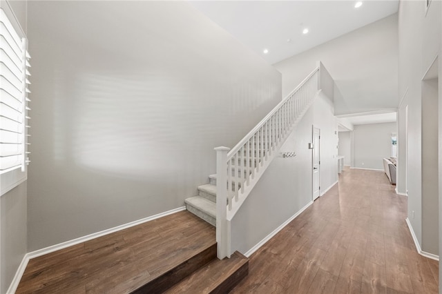 stairs featuring baseboards, wood finished floors, a high ceiling, a wealth of natural light, and recessed lighting