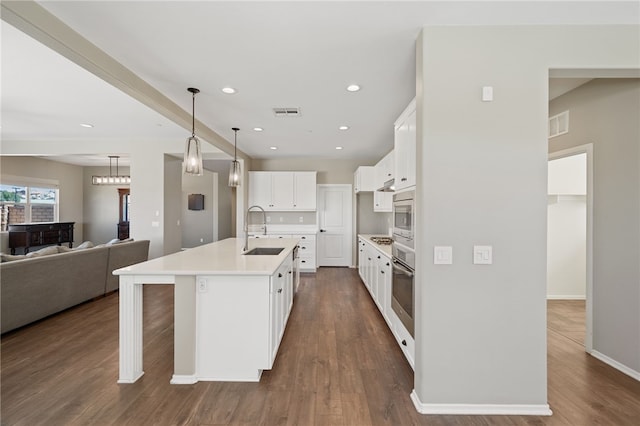 kitchen featuring light countertops, open floor plan, white cabinetry, a sink, and an island with sink