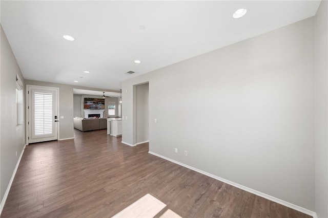 unfurnished living room featuring a warm lit fireplace, baseboards, wood finished floors, and recessed lighting