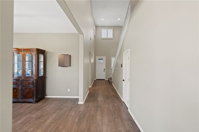 corridor with recessed lighting, a high ceiling, baseboards, and wood finished floors