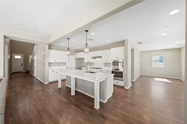 kitchen with white cabinets, light countertops, appliances with stainless steel finishes, hanging light fixtures, and a center island with sink