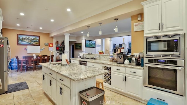 kitchen with appliances with stainless steel finishes, decorative light fixtures, white cabinetry, a center island, and light stone countertops