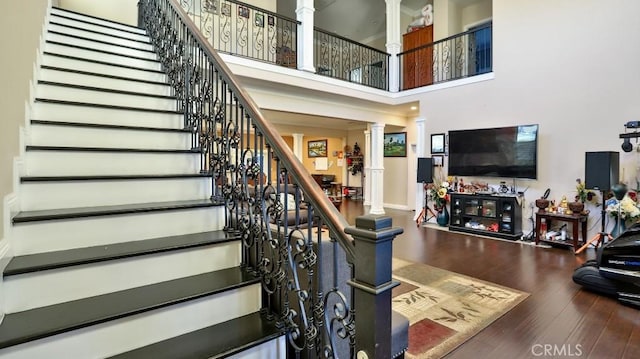 staircase featuring ornate columns, a high ceiling, and hardwood / wood-style floors