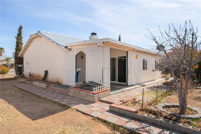 rear view of house with stucco siding, a chimney, and fence