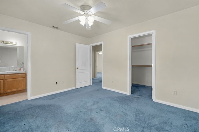 unfurnished bedroom with light colored carpet, baseboards, visible vents, a walk in closet, and ensuite bathroom