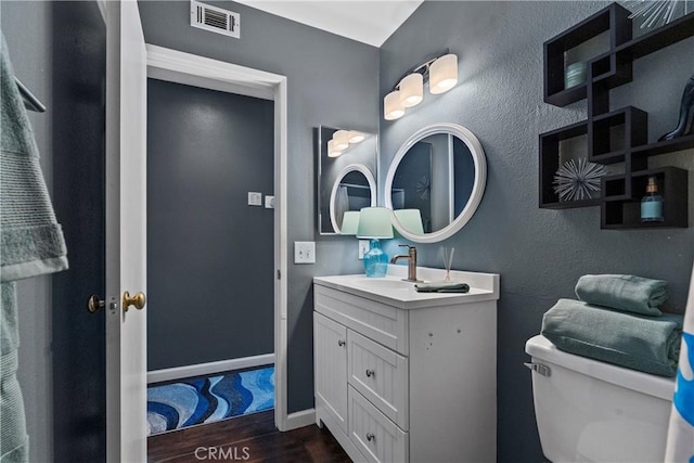 bathroom with toilet, wood finished floors, vanity, visible vents, and baseboards