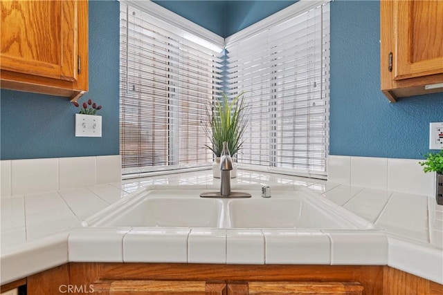 interior details featuring tile counters, brown cabinets, a textured wall, and a sink