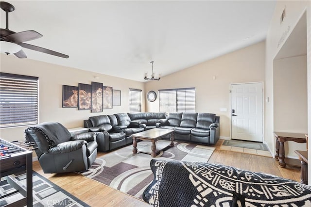 living area with vaulted ceiling, ceiling fan with notable chandelier, light wood-type flooring, and baseboards