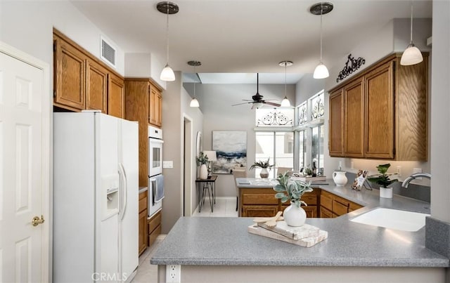 kitchen with a peninsula, white appliances, brown cabinetry, and a sink