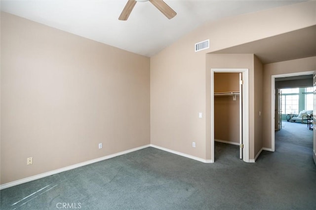 unfurnished bedroom featuring lofted ceiling, visible vents, dark carpet, a spacious closet, and baseboards