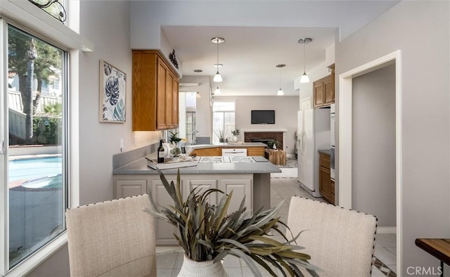 kitchen with a peninsula, white fridge with ice dispenser, brown cabinets, and decorative light fixtures