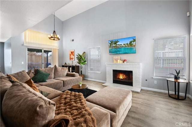 living room featuring a brick fireplace, high vaulted ceiling, hardwood / wood-style floors, and a chandelier