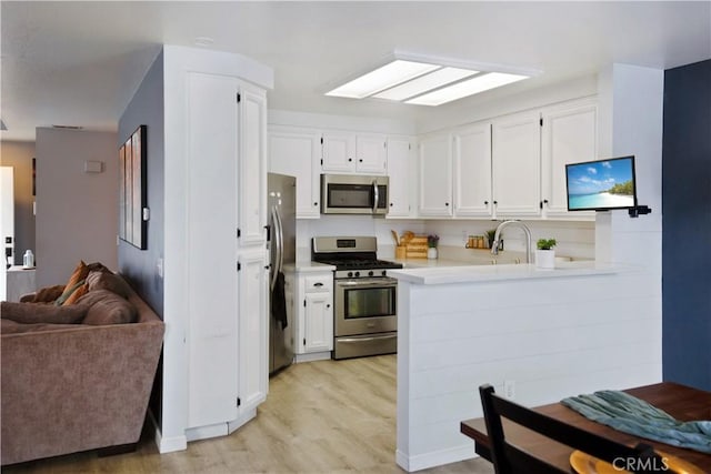 kitchen featuring sink, light hardwood / wood-style flooring, kitchen peninsula, stainless steel appliances, and white cabinets