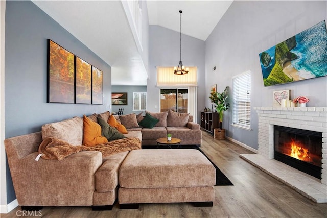 living room with wood-type flooring, a brick fireplace, an inviting chandelier, and high vaulted ceiling