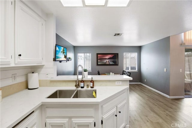 kitchen featuring white cabinetry, sink, light hardwood / wood-style floors, and kitchen peninsula