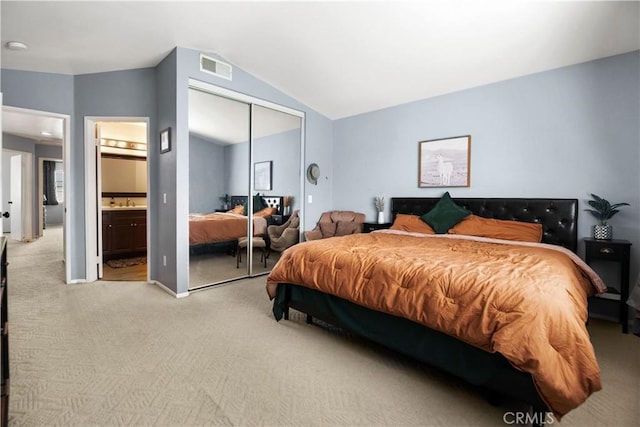 bedroom featuring a closet, connected bathroom, vaulted ceiling, and light carpet