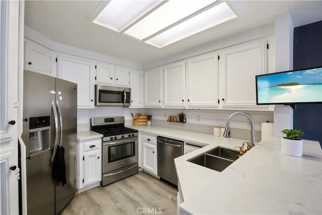 kitchen featuring appliances with stainless steel finishes, sink, white cabinets, and light wood-type flooring