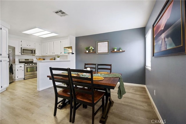 dining room featuring a skylight and light hardwood / wood-style flooring