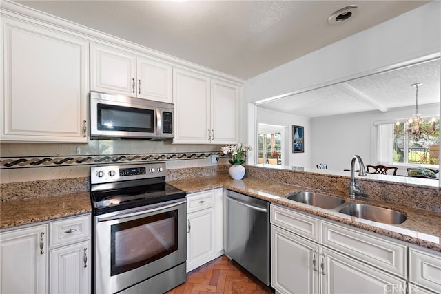 kitchen featuring appliances with stainless steel finishes, white cabinetry, a sink, and dark stone countertops