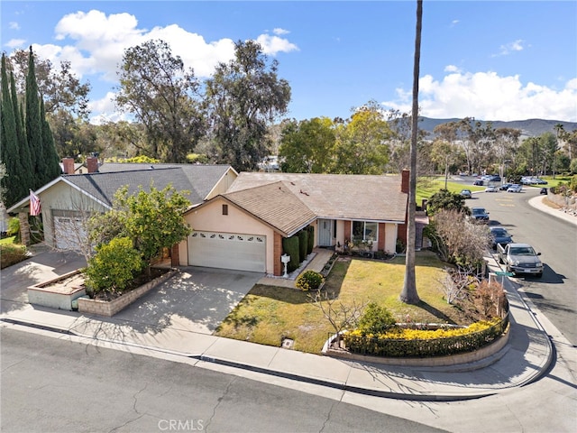 ranch-style home with driveway, an attached garage, a mountain view, and a front yard