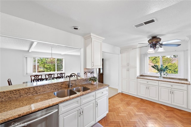 kitchen featuring visible vents, dishwasher, light stone counters, white cabinetry, and a sink