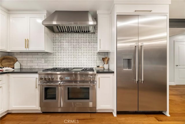 kitchen featuring light wood-style floors, dark countertops, wall chimney range hood, and high quality appliances