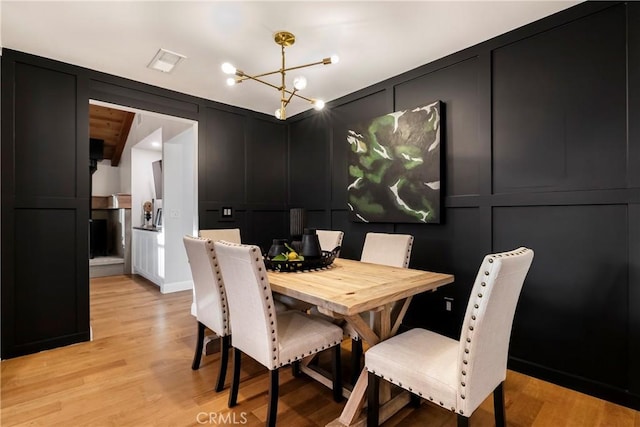 dining room with visible vents, an inviting chandelier, light wood-style flooring, and a decorative wall