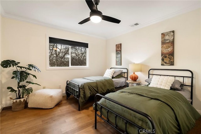 bedroom with ornamental molding, a ceiling fan, visible vents, and wood finished floors