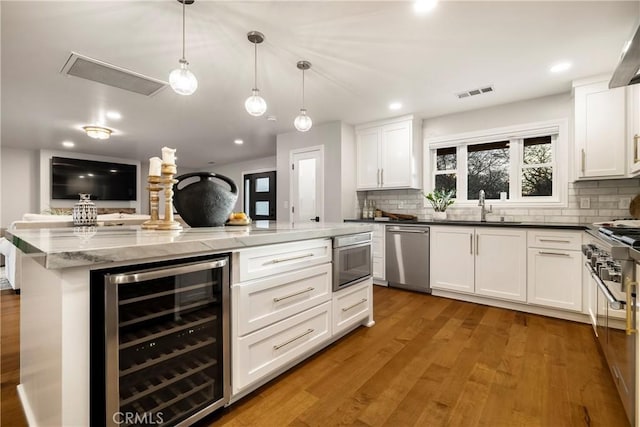 kitchen featuring visible vents, decorative backsplash, appliances with stainless steel finishes, a sink, and beverage cooler