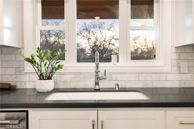 interior space with tasteful backsplash, dark countertops, a sink, and white cabinets