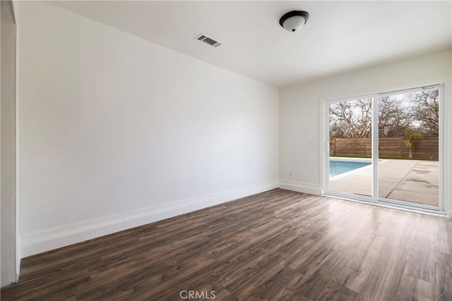 empty room with dark wood-style floors, visible vents, and baseboards