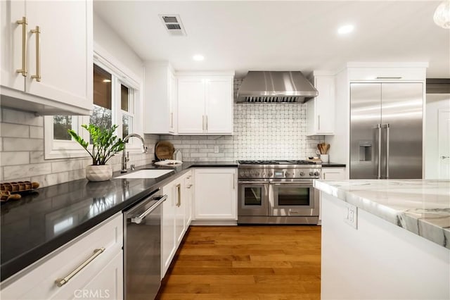 kitchen with light wood finished floors, visible vents, high end appliances, wall chimney exhaust hood, and a sink