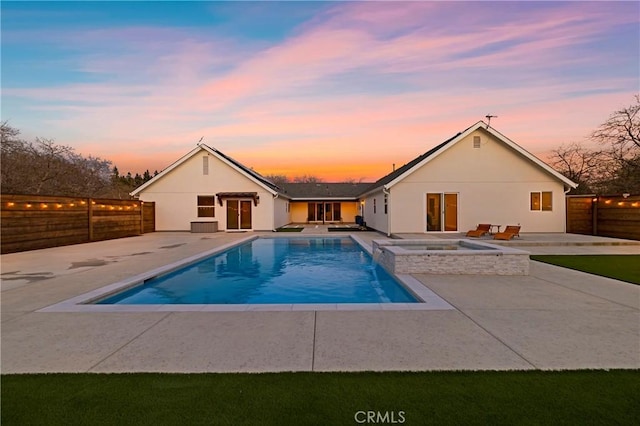 pool at dusk with a pool with connected hot tub, a patio area, and a fenced backyard