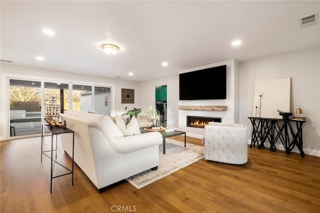 living area with a warm lit fireplace, visible vents, wood finished floors, and recessed lighting