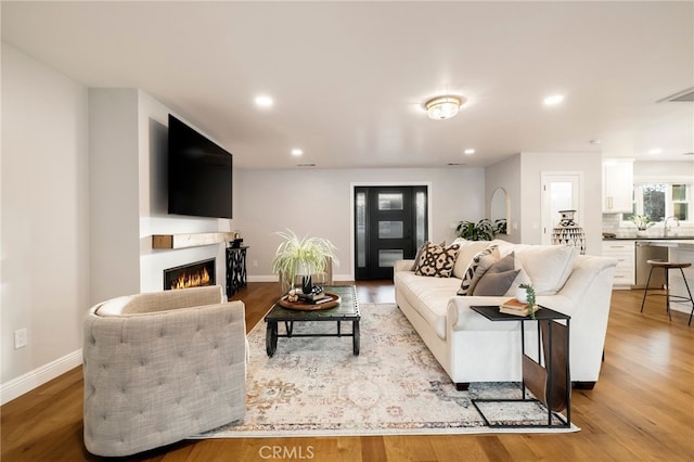 living room featuring a warm lit fireplace, light wood-style flooring, and baseboards