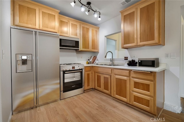 kitchen featuring light wood finished floors, appliances with stainless steel finishes, light countertops, and a sink