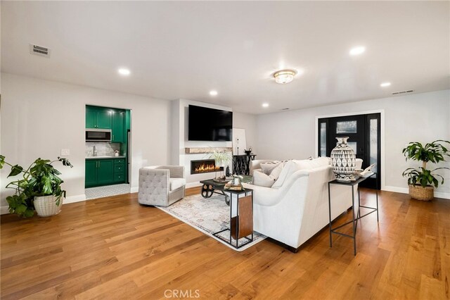 living room with recessed lighting, visible vents, baseboards, light wood-style floors, and a lit fireplace