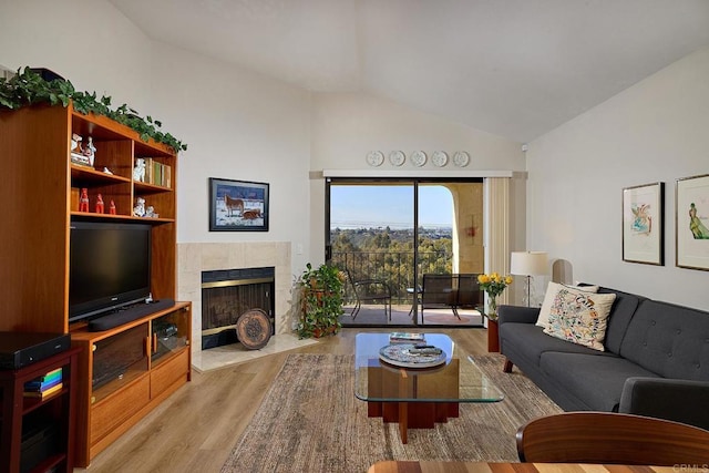 living room featuring light hardwood / wood-style flooring, vaulted ceiling, and a tiled fireplace