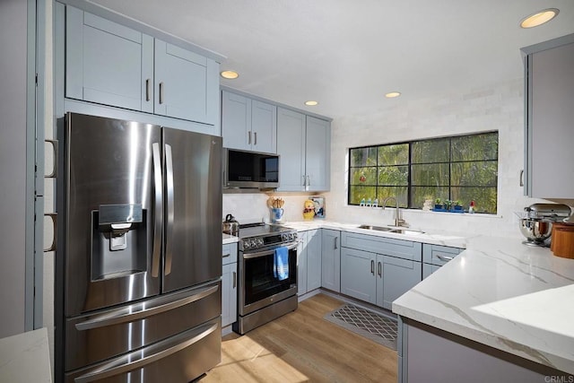 kitchen featuring gray cabinetry, light hardwood / wood-style floors, sink, light stone counters, and appliances with stainless steel finishes