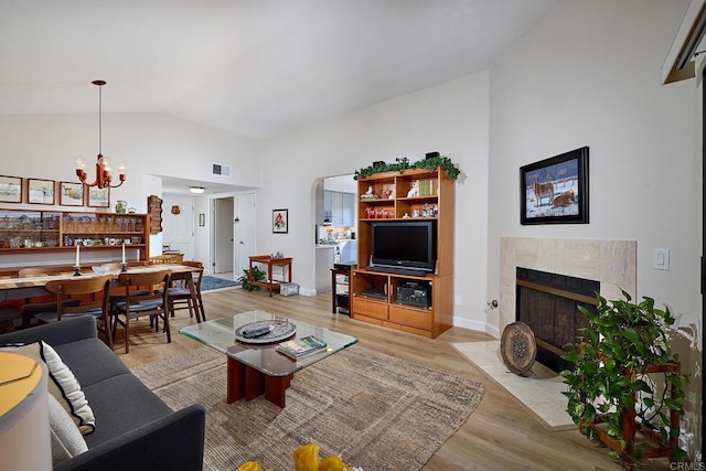 living room with a high end fireplace, high vaulted ceiling, a notable chandelier, and light hardwood / wood-style flooring