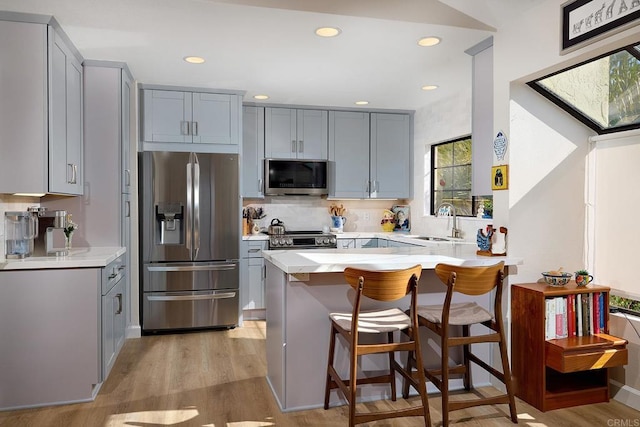 kitchen with gray cabinets, a kitchen bar, stainless steel appliances, and kitchen peninsula