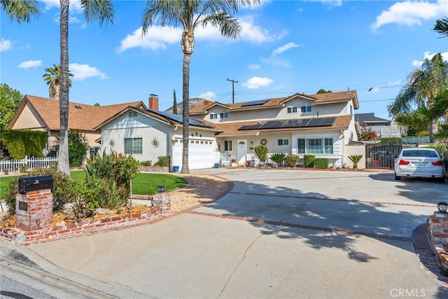 view of front facade with driveway, fence, an attached garage, and solar panels