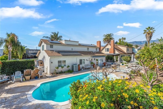 rear view of property featuring central AC unit, a patio, solar panels, and a fenced in pool