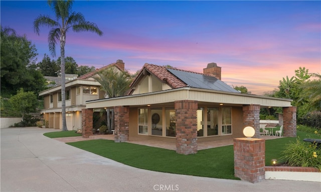 back of house with a garage, a lawn, a chimney, concrete driveway, and solar panels