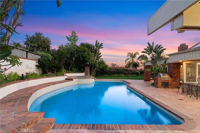 view of swimming pool with a patio, fence, a pool with connected hot tub, and exterior kitchen