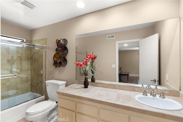 bathroom featuring toilet, visible vents, shower / bath combination with glass door, and vanity