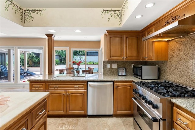 kitchen with tasteful backsplash, a sink, appliances with stainless steel finishes, range hood, and brown cabinetry