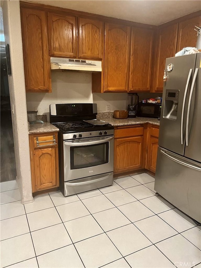 kitchen featuring brown cabinetry, appliances with stainless steel finishes, under cabinet range hood, and dark countertops