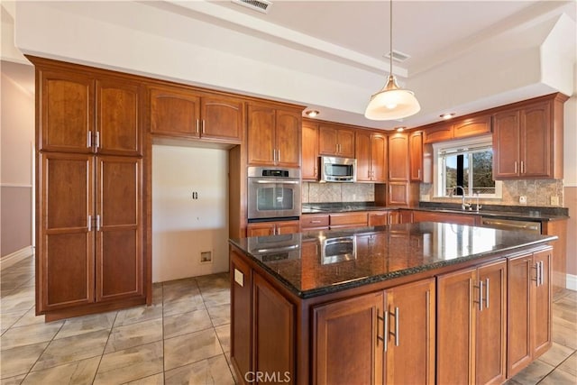 kitchen with dark stone countertops, appliances with stainless steel finishes, pendant lighting, a kitchen island, and tasteful backsplash