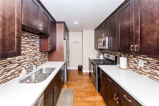 kitchen featuring light wood-type flooring, stainless steel appliances, dark brown cabinetry, backsplash, and sink